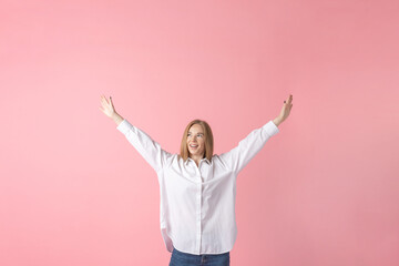 Lifestyle concept. Joyful woman with arms raised in a white shirt and blue jeans against a pink backdrop