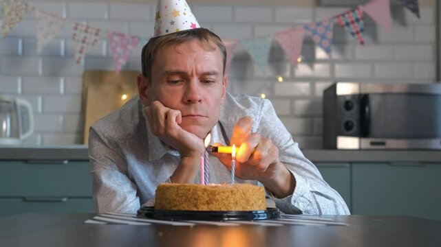 On a quiet birthday, a lonely man gazes longingly at his cake, lighted candles flickering as he tastes the frosting from his finger, embracing a bittersweet moment of solitude