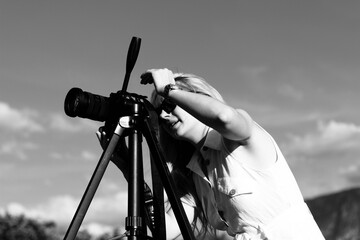 A woman photographer adjusts the camera for shooting. Black and white photo of a beautiful blonde...