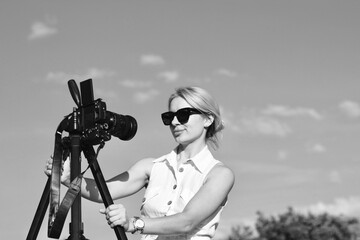 A woman photographer adjusts the camera for shooting. Black and white photo of a beautiful blonde...