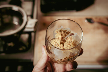 A glass filled with ice cubes and powdered Amanita muscaria mushroom on its surface, held in the hand, illuminated by natural sunlight. Preparing a homemade fly agaric elixir