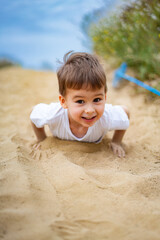 Boy playing in sand by the water. A joyful young boy crawls through the soft sand by the water, enjoying a sunny day outdoors and embracing playful activities.