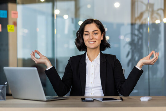 Confident woman in business suit practicing mindfulness yoga pose at office desk. Promotes calmness and focus during work. Ideal for themes related to meditation, stress management, and wellness.