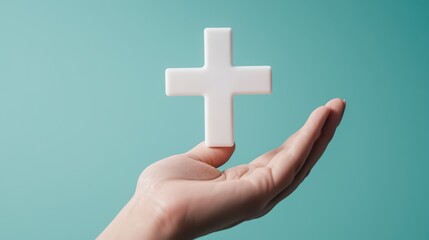 Obraz premium Hand holding a white cross symbol against a turquoise background.