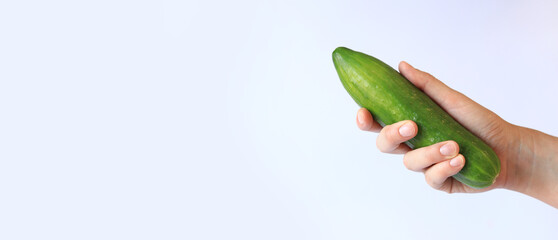 Cucumber in a female hand on a light background. Close-up of a hand with a cucumber. Harvest. Healthy eating and diet concept. Vegetables. White female hand shows a fresh tasty cucumber