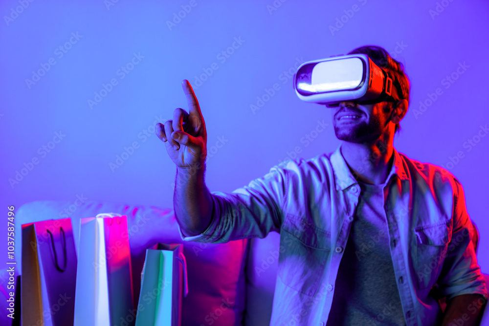 Poster caucasian man with vr glass posing pointing finger while sitting at sofa with shopping bags. person 