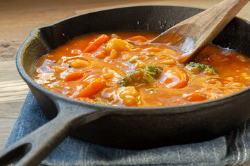 Homemade vegetable soup in a cast iron frying pan on a tea towel with a wooden spoon.