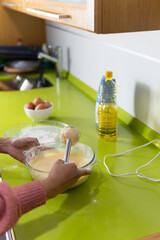 unrecognizable woman's arms prepare liquid sponge cake batter on lime green kitchen counter with eggs, sunflower oil, bowl and mixer. 4