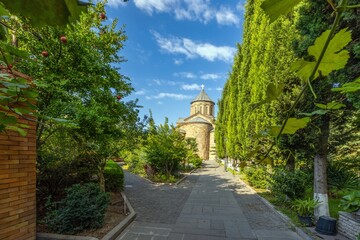 Garden of the Metekhi Church in Tbilisi, Georgia, with greenery and clear skies on a sunny day