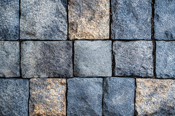 Fototapeta premium Square stone tiles in varying shades of gray and beige arranged in a grid pattern showcasing a rough and textured surface 