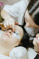 Girl cosmetologist laminates and paints woman eyelashes