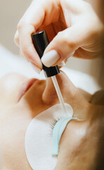 Girl cosmetologist laminates and paints woman eyelashes