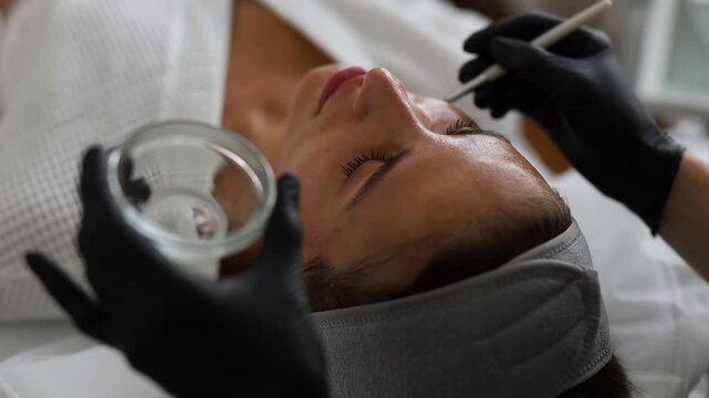 Cosmetologist performs a facial peeling procedure on a young woman.