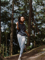 Joyful young woman jogging through lush green forest, wearing comfortable sportswear, enjoying nature and staying active Fitness and outdoor adventure concept