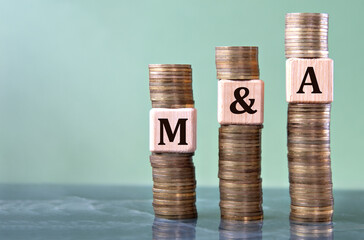 M and A - acronym on wooden cubes on stacks of coins
