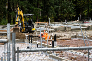 New construction started in a mixed use commercial and industrial zone, cleared job site with foundation started, heavy equipment and workers behind chain-link fence
