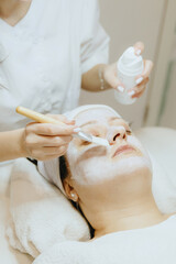 A girl cosmetologist applies a cream mask with a brush to a woman face.