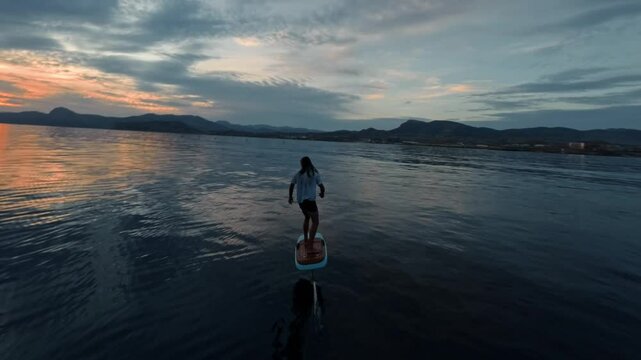 Man glides on hydrofoil board on water surface of sea against the background of beautiful golden sunset sky. High quality FullHD footage
