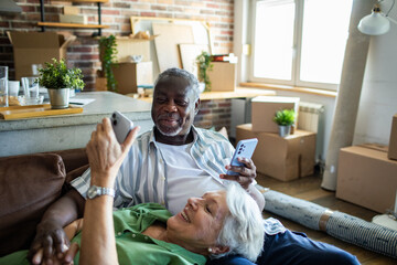 Senior couple relaxing on couch with smartphones after moving in