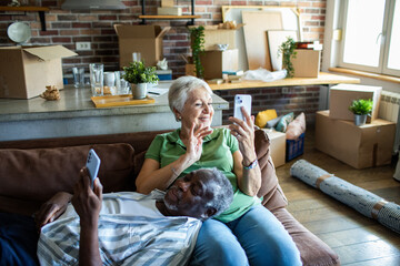 Senior couple relaxing on couch with smartphones after moving in