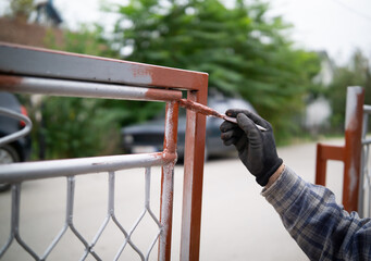 Male hand painting metal fence with a brush with red oxide metal primer