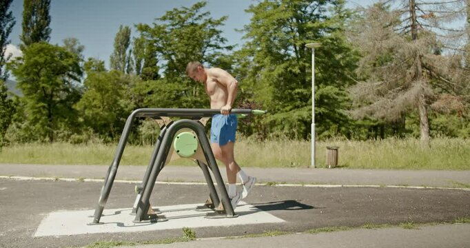 A muscular man performs dips on the parallel bars in a park workout. He takes a break, leaning on the bars. Fitness and exercise are important for health and well-being.