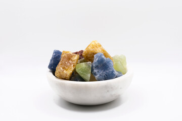 An image of several small multicolored healing calcite crystals in a white bowl. 