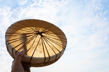 An image of a handmade leather meditation drum being held up against a cloudy blue sky. 