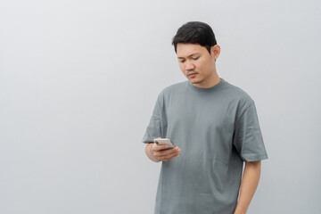 Sad and disappointed expression of adult Asian man using mobile phone with casual t-shirt isolated...