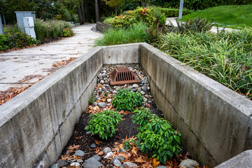 Rusty raised square iron stormwater drain surrounded by small rocks and plants, lower than ground...