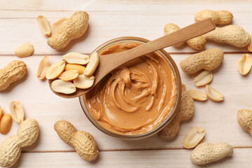 Tasty peanut butter in bowl and nuts on wooden table, flat lay