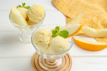 Scoops of melon sorbet with mint and fresh fruit in glass dessert bowls on white wooden table, closeup
