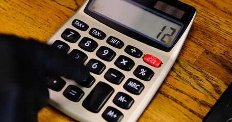 A hand wearing a black glove counts cash using an old-fashioned calculator capturing the meticulous process of managing finances showcasing the contrast between modern and traditional methods.