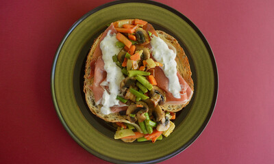 Toasted sourdough ciabatta bread with prosciutto, tzatziki and pan fired vegetables on a plate.
