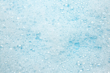 Washing laundry. White foam with bubbles on light blue background, top view