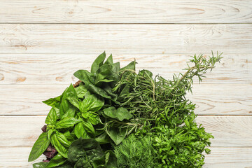 Different fresh herbs in basket on white wooden table, top view. Space for text