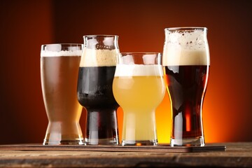 Glasses with different types of beer on wooden table against color background