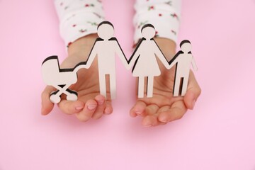 Adoption. Little girl with figures of family on pink background, closeup