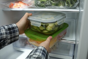 Woman taking glass containers with frozen vegetables from refrigerator, closeup