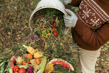 Compost heap pile with bio waste. Farmer hands put weeds grass plants, vegetable fruit scraps from...
