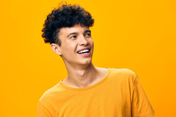 Young man with curly hair smiling against a vibrant yellow background, radiating joy and positivity...