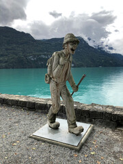 A wooden sculpture of a mountain climber, with a backpack, is walking on the sidewalk along Lake Brienz in Switzerland