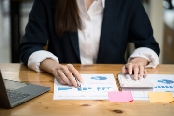 Close up of hands typing on laptop keyboard and working on document paperwork and calculator for cost financial marketing