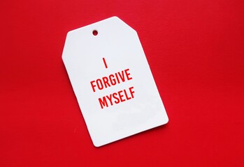 White tag on red background with message text I FORGIVE MYSELF, positive affirmation of learning to...