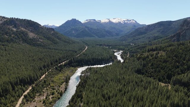 aerial shot of the Caleuf&uacute; River winding through the lush pine forests in Villa Meliquina, Argentina. The landscape is dominated by vast green forests, including pines, coihue, and lenga trees.