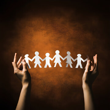 Hands holding a paper chain of people figures against an orange background, symbolizing unity and teamwork.