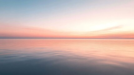 A calm sea at sunrise, with soft pink and orange hues reflecting on the still water