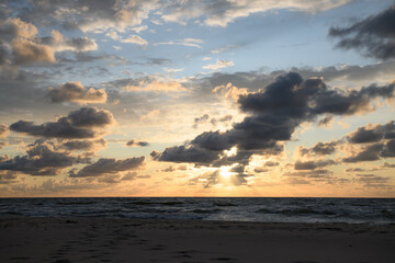 As the sun gently descends toward the horizon, the picturesque ocean reflects the vibrant hues of the clouds in the sky above