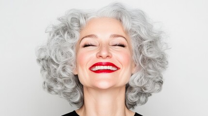 A middle-aged woman with curly silver and gray hair laughing joyfully and looking slightly upwards with her eyes closed, her expression radiating pure happiness, against a white background.