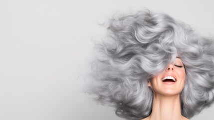 A playful moment as a woman tosses her curly silver and gray hair back while laughing with delight, captured candidly with a clean white background.